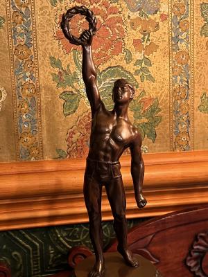 [bronze sculpture: nude male arm stretched upward with wreath]